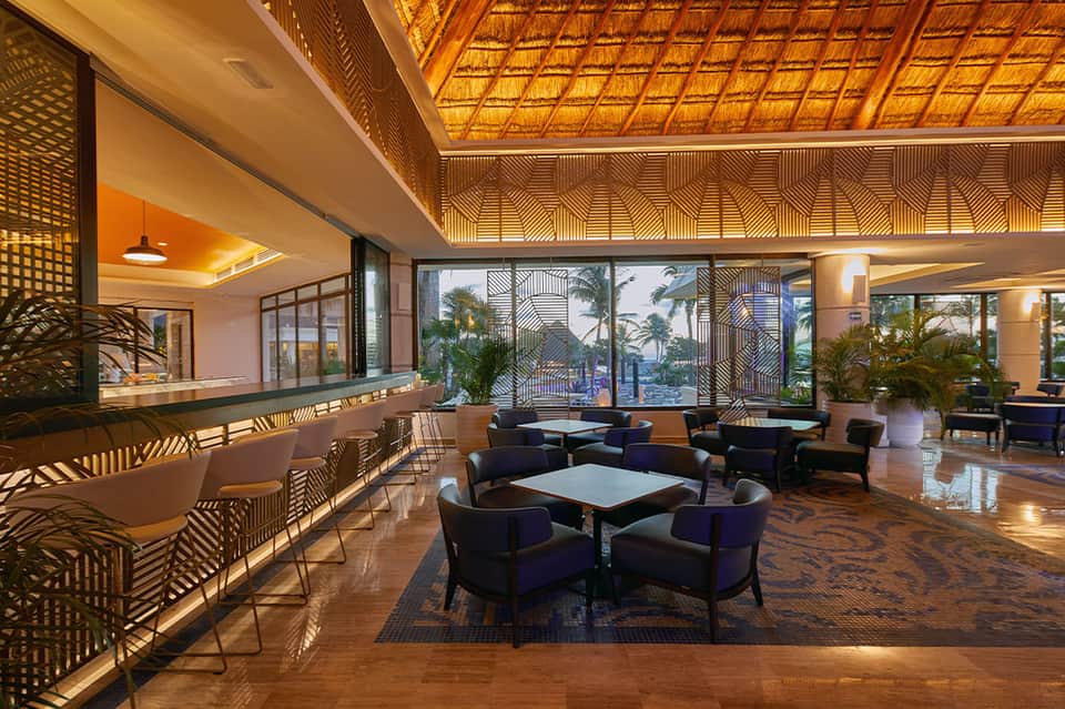 Upscale hotel lobby with geometric wood ceiling details, ocean view windows, and modern seating arrangements