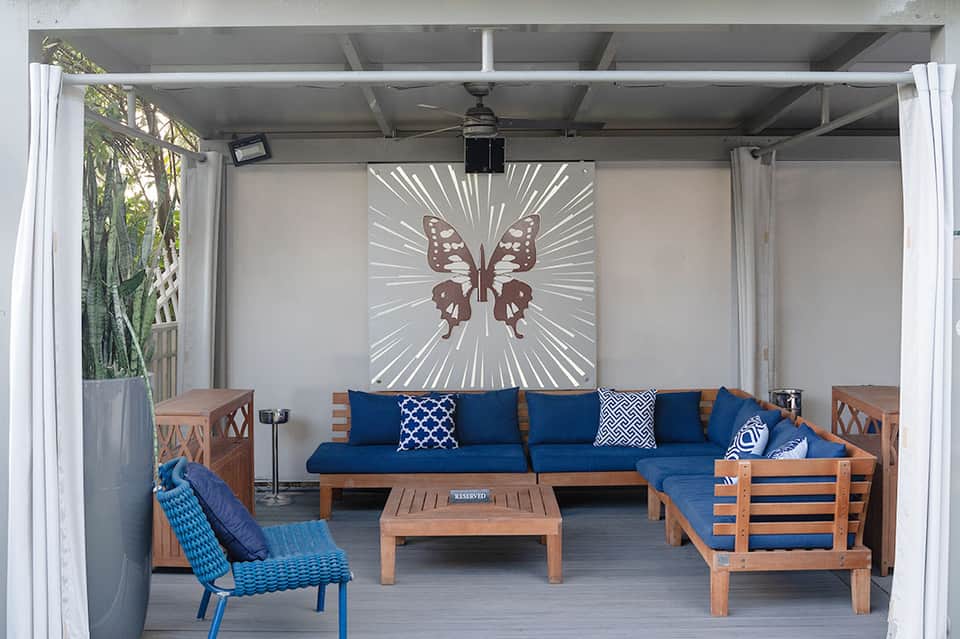 Covered pavilion with wooden furniture, blue cushions, and butterfly wall art