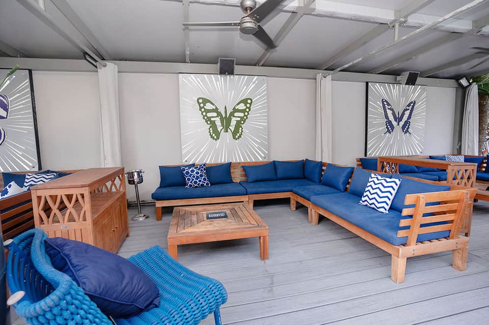 Covered patio lounge with blue cushioned wooden seating, butterfly art panels, and wooden table