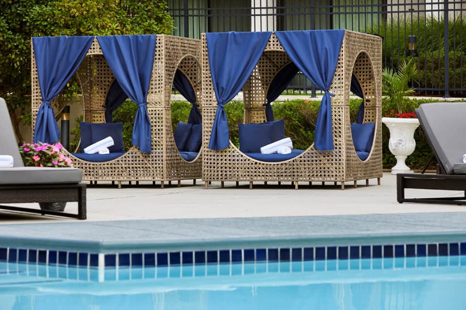 Woven cabanas with blue curtains and cushions positioned beside resort swimming pool
