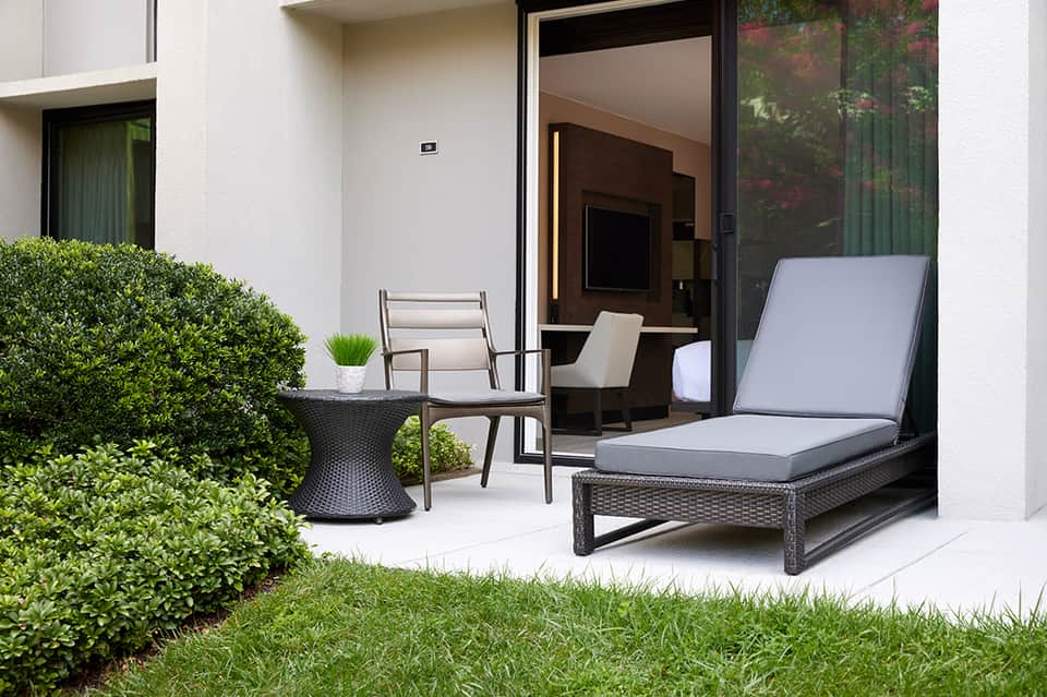 Modern patio with black rattan lounger, chair, side table, and manicured hedges
