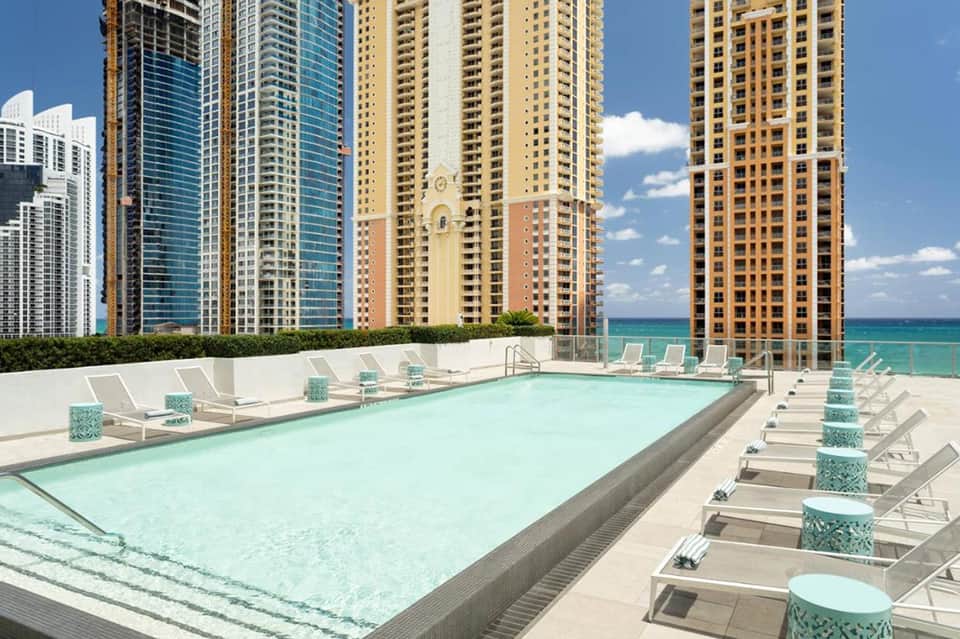 Rooftop pool overlooking ocean with high-rise buildings and white loungers
