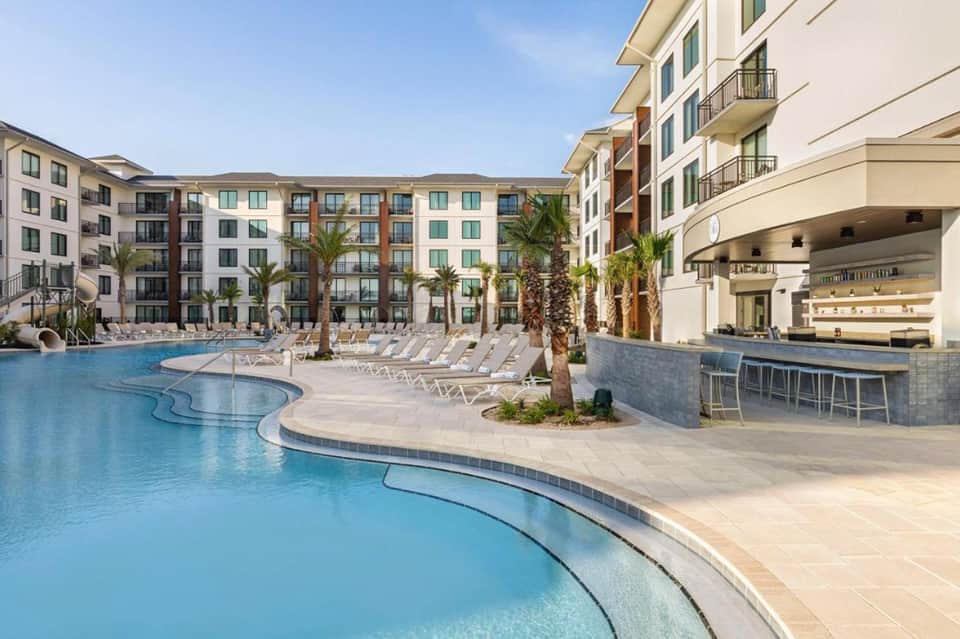 Resort courtyard with curved pool, palm trees, apartment buildings, and poolside bar