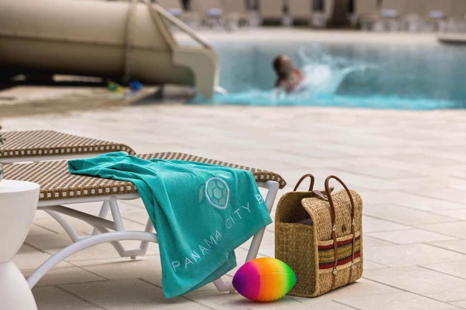 Poolside scene with colorful beach towel, straw bag, and beach ball on lounge chair