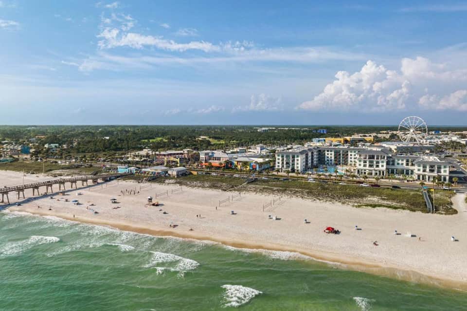 Beachfront view with sandy shore, ocean waves, Ferris wheel, and coastal resort buildings