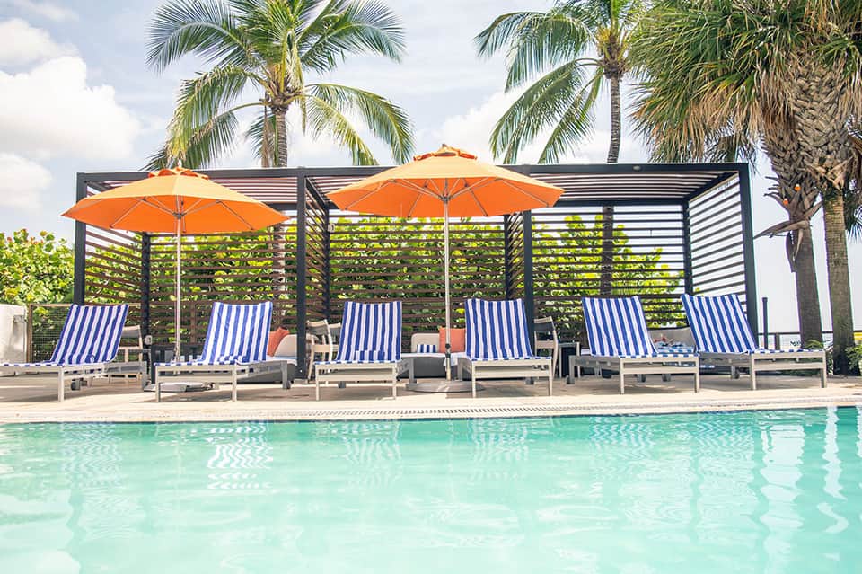 Pool lounge with striped chaise lounges, orange umbrellas, and palm trees
