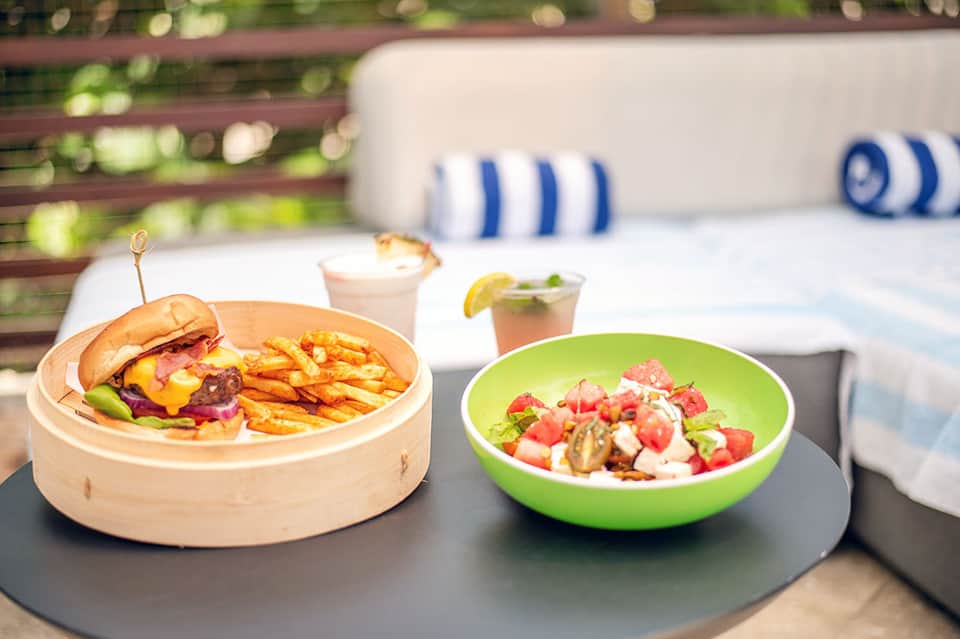 Casual dining plate with gourmet burger, fries, and fresh salad by poolside