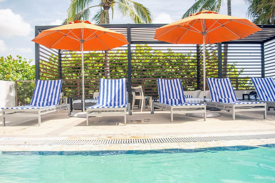 Lounge chairs with blue and white striped cushions under orange umbrellas by pool