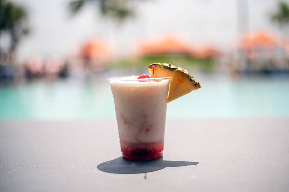 Tropical cocktail with pineapple garnish on sandy beach with pool in background