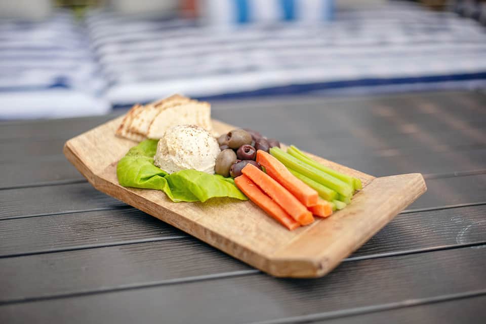 Appetizer platter with hummus, fresh vegetables, crackers, and olives on wooden board