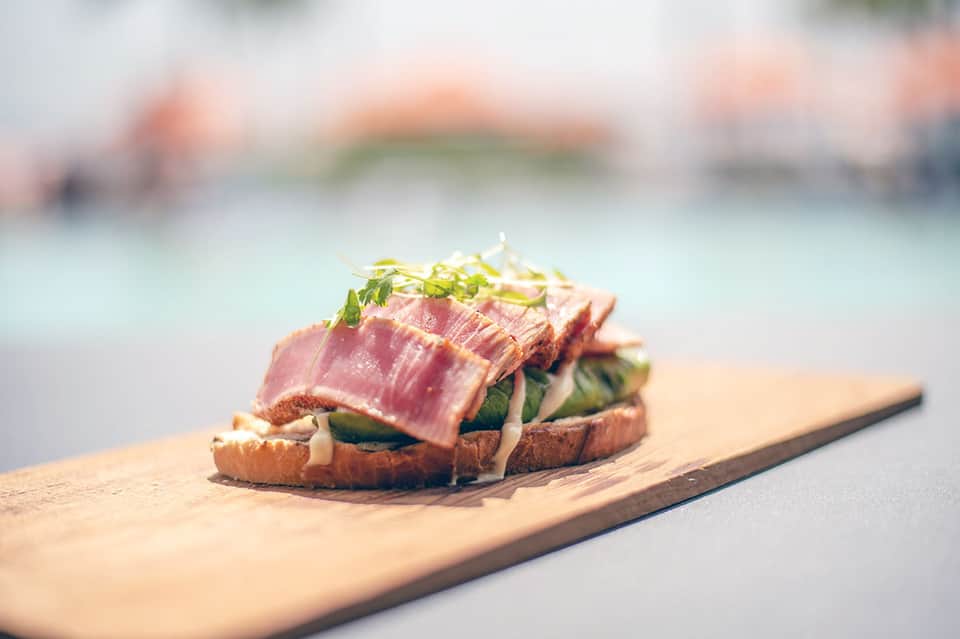 Seared tuna sandwich on wooden board with ocean and beach blurred in background