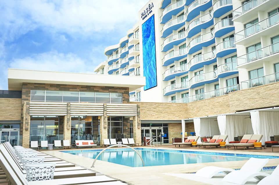 Modern beachfront hotel with curved balconies, blue and white striped design, and outdoor swimming pool with lounge chairs