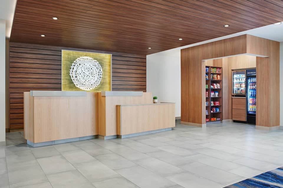 Modern hotel lobby with wood paneling, light wood reception desks, and vending machine area.