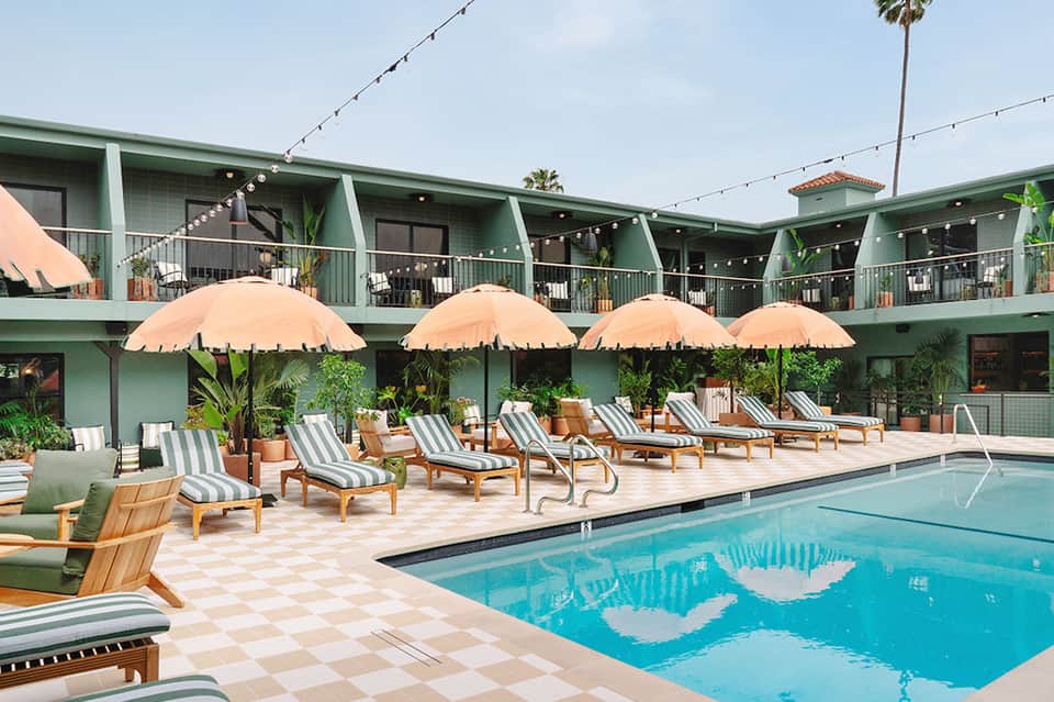 Resort pool with peach umbrellas, striped loungers, green building facade, and string lights