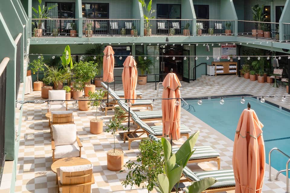 Resort pool with striped loungers under coral umbrellas and mint green building backdrop