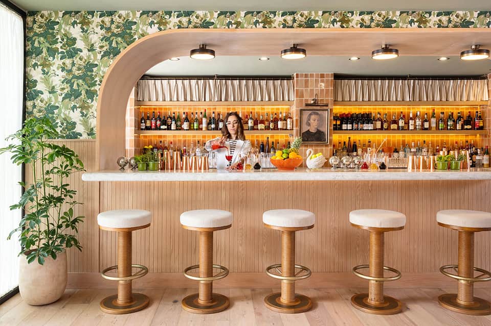 Modern hotel bar with botanical wallpaper, wooden stools, and well-stocked liquor shelves
