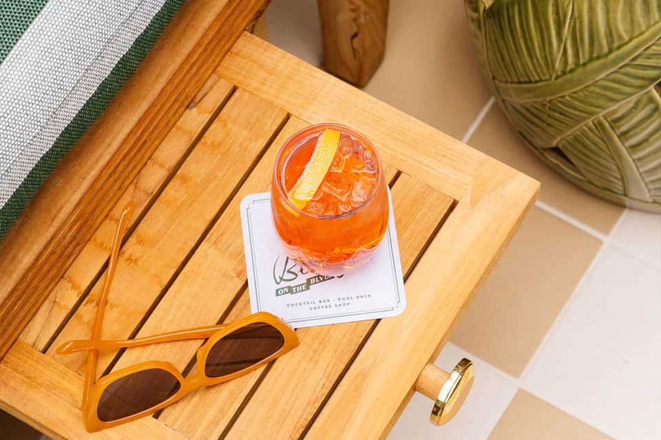 Colorful cocktail on wooden table with sunglasses, green foliage, pool deck ambiance