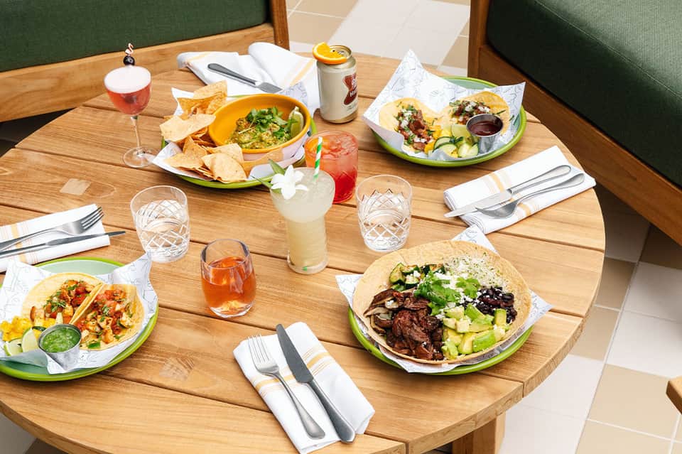 Colorful Mexican cuisine and cocktails served at wooden table with green booth seating in casual restaurant setting