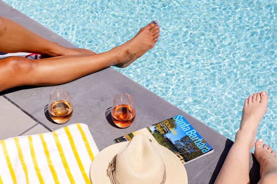 Person relaxing poolside with legs extended, drinks on table, striped towel nearby