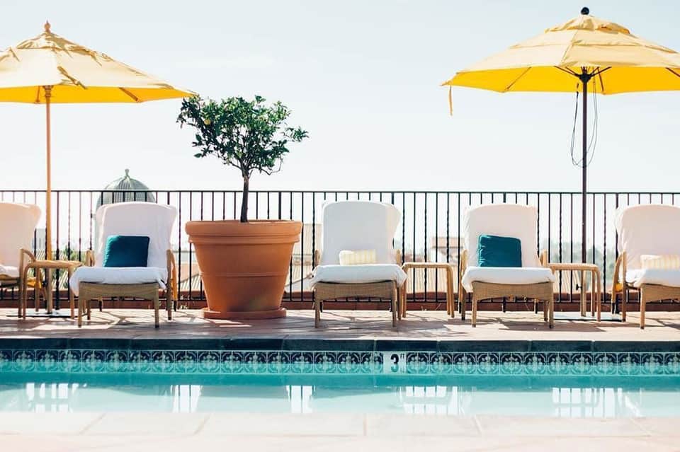 Resort poolside lounge area with white chairs, yellow umbrellas, and ocean view beyond the railing