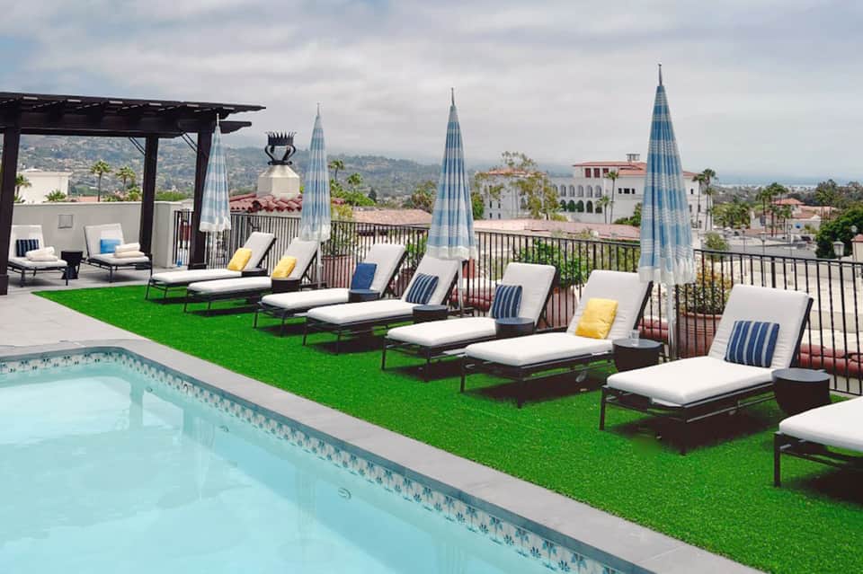 Rooftop pool overlooking hillside with lounge chairs on artificial turf and city skyline
