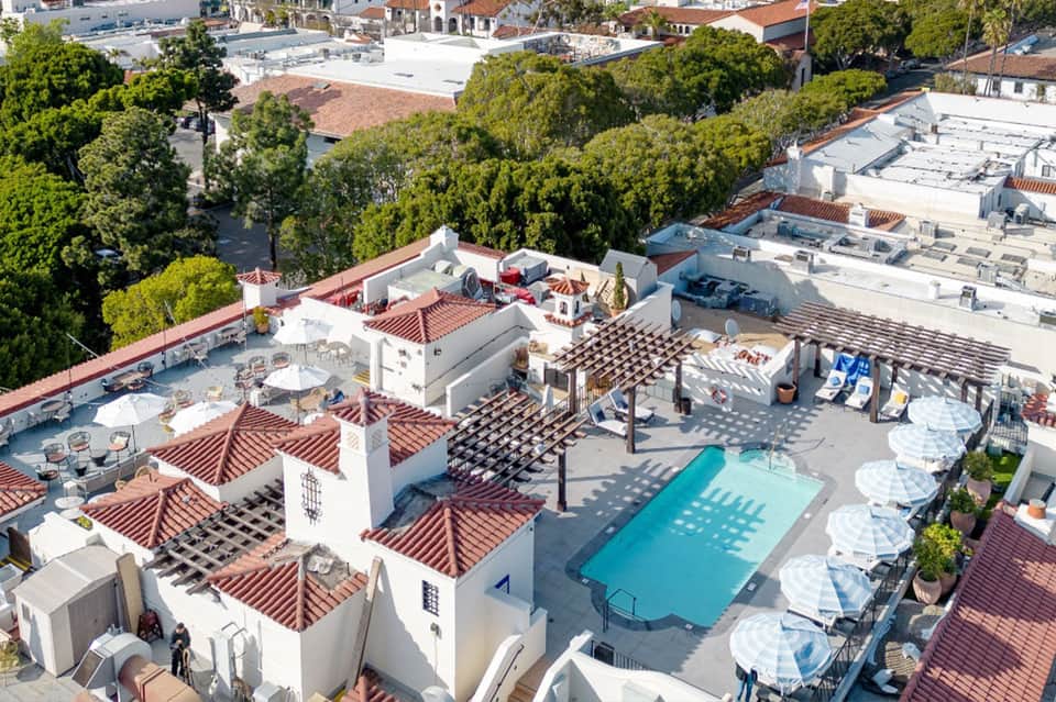 Aerial view of Spanish-style rooftop pool area with white umbrellas, terracotta tiles, and surrounding buildings