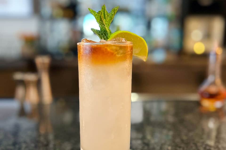 Craft cocktail with amber liquid, fresh lime wheel, and mint sprig on bar counter