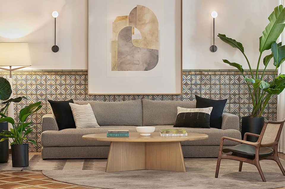 Modern lounge interior with gray sofa, decorative artwork, patterned tile accent wall, and potted plants