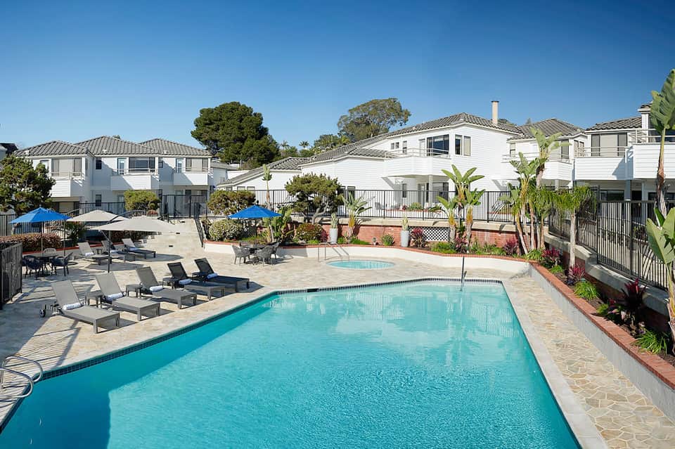 Community resort pool with turquoise water, lounge chairs, white residential buildings, and landscaping