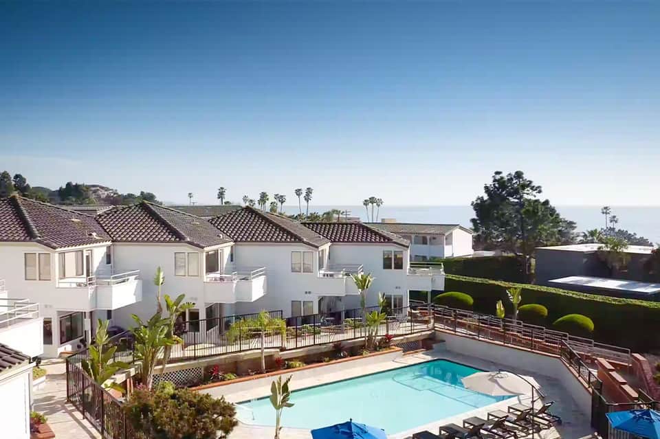 Hillside townhomes with light blue pool, red tile roofs, and ocean view beyond the property