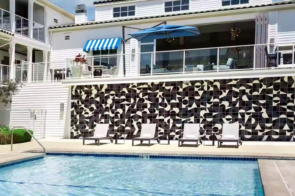Modern beach house with white exterior, black and white tile wall, pool and blue umbrella