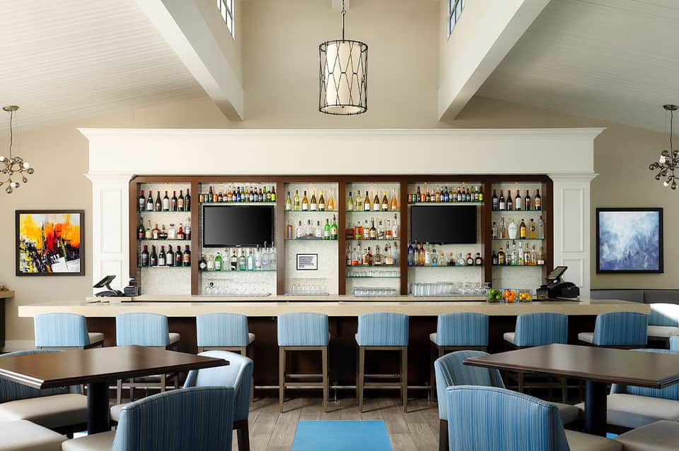 Modern bar lounge with extensive liquor shelves, blue bar seating, and high ceiling