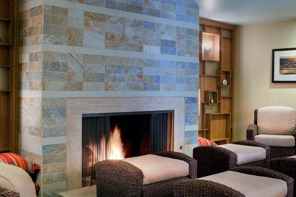 Elegant lounge with stone fireplace, wicker seating, decorative pillows, and framed ocean artwork