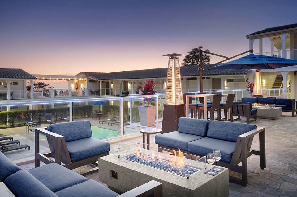 Luxury modern home with infinity pool, fire pit seating area, and illuminated design at dusk