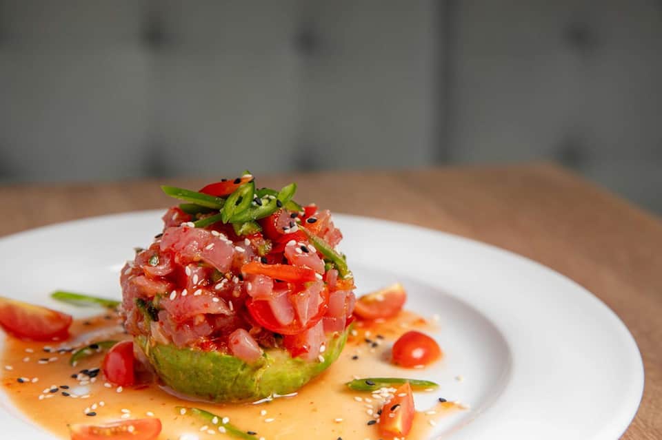 Plated seafood dish with tuna tartare, avocado, sesame seeds, and spicy mayo sauce