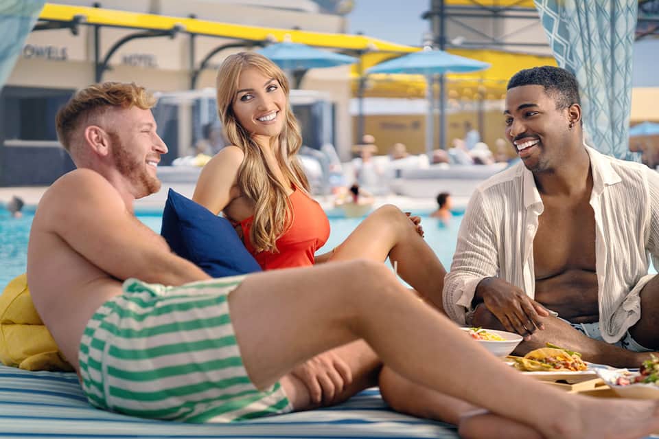 Guests socializing poolside at vibrant resort with yellow umbrellas and colorful pool floats