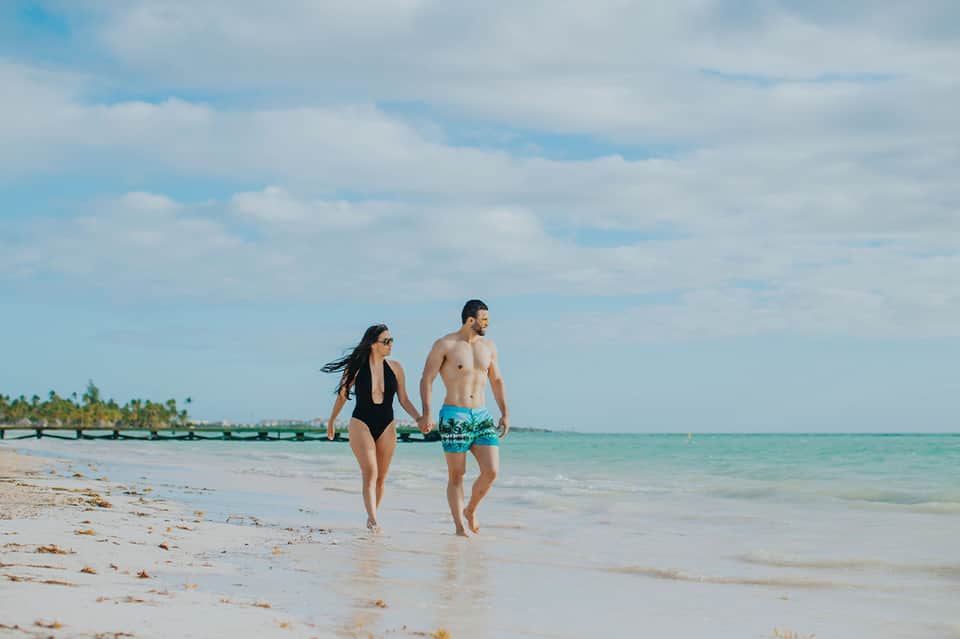 Couple walking hand-in-hand on sandy beach with clear turquoise water and tropical scenery