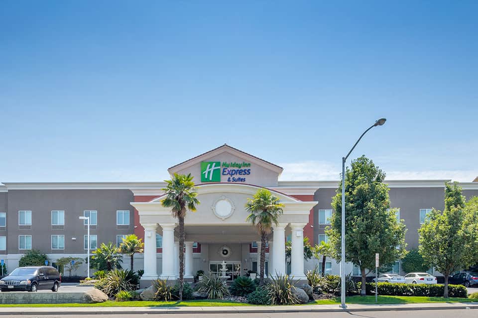 Holiday Inn Express exterior with cream and red facade, palm trees, and parking lot