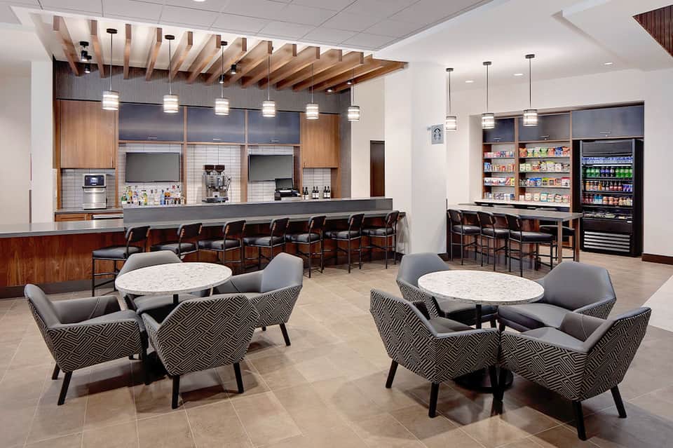 Modern hotel lounge with bar, seating areas, and beverage station