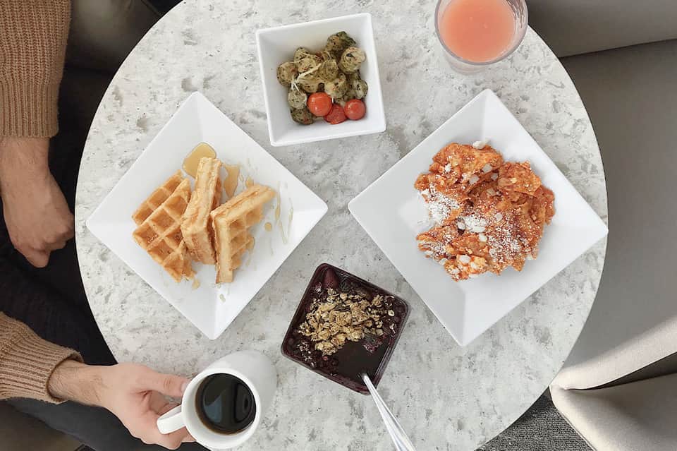 Dessert spread on marble table with waffles, pastries, fruits, and tropical beverage