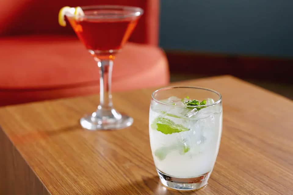 Two cocktails on wooden table: red martini and white mint mojito with colored background