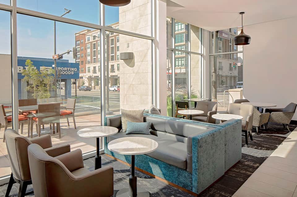 Contemporary lounge with turquoise accent sofa, floor-to-ceiling windows, and urban city view