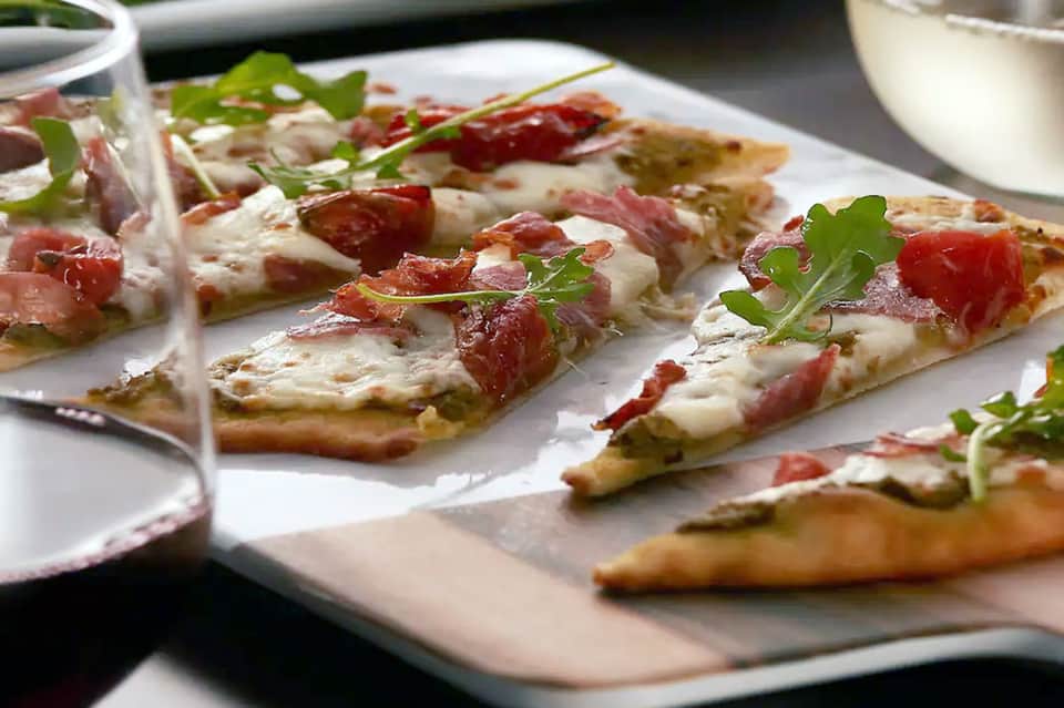Gourmet appetizers on white plate with prosciutto, cheese, and fresh herb garnish