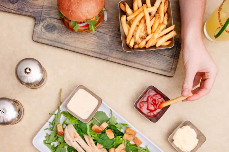 Overhead food spread featuring burger, fries, salad, and condiments on a table