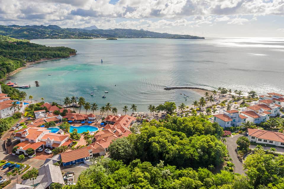 Aerial view of tropical beach resort with blue pool, palm trees, and turquoise bay