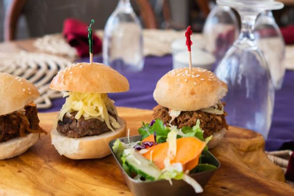Gourmet sliders with beef patties, toppings, and colorful skewers on wooden serving board