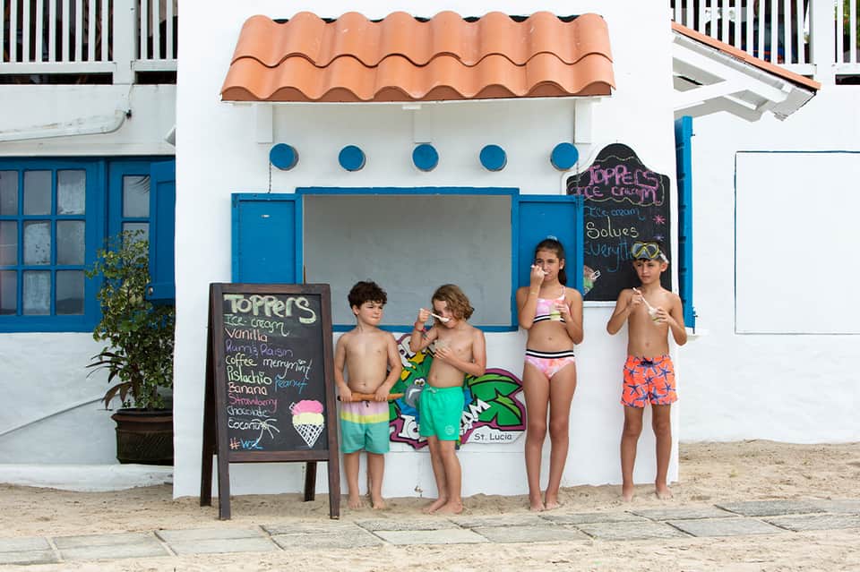 Four children eating ice cream at beach-side ice cream shop with blue and white facade