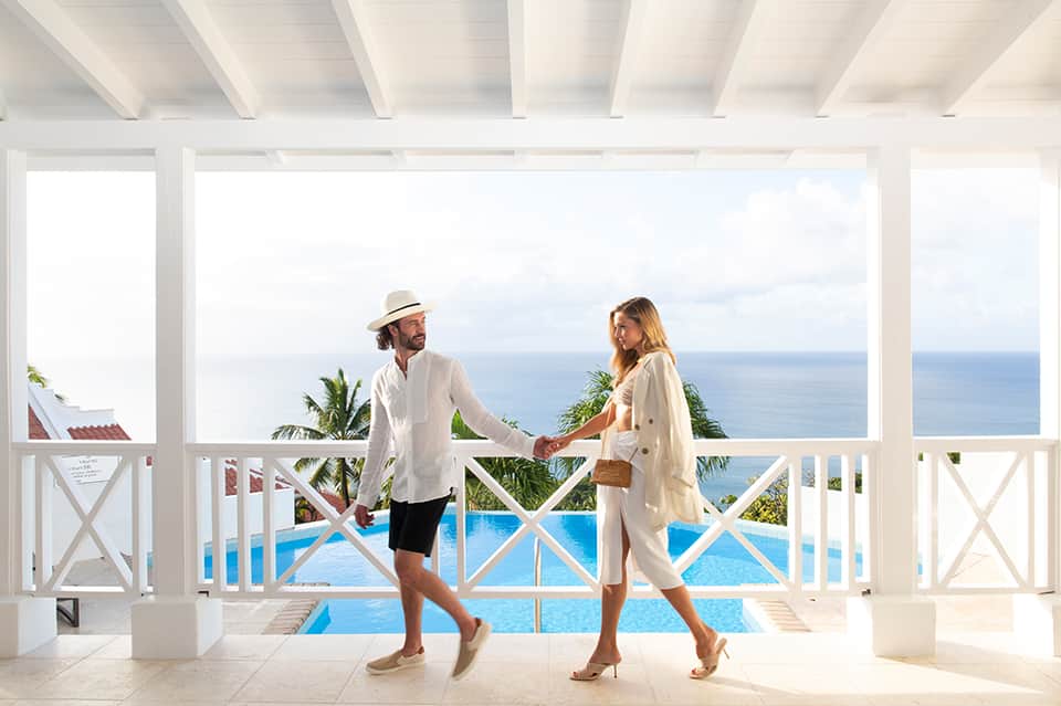 Couple on oceanview terrace with white railings, infinity pool, and sea horizon