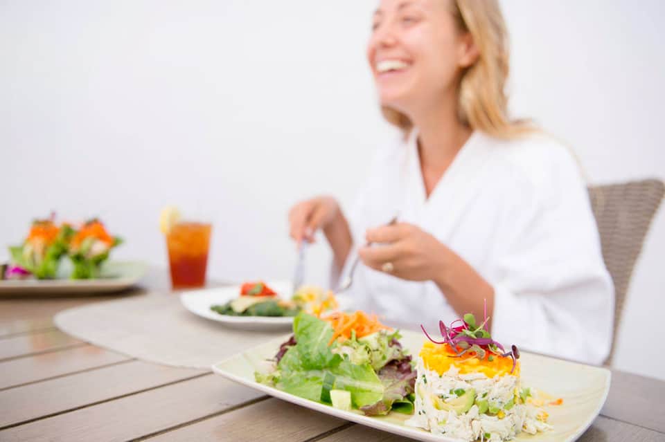 Woman dining outdoors with colorful salad plate and tropical beverage at resort restaurant