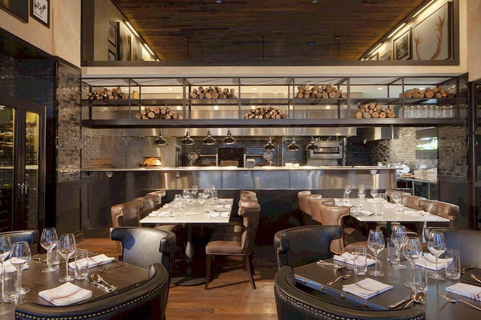 Upscale restaurant dining room with open kitchen, pendant lights, wood accents, and booth seating